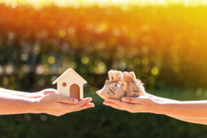 Two hands holding a house and money bags, symbolising wealth.