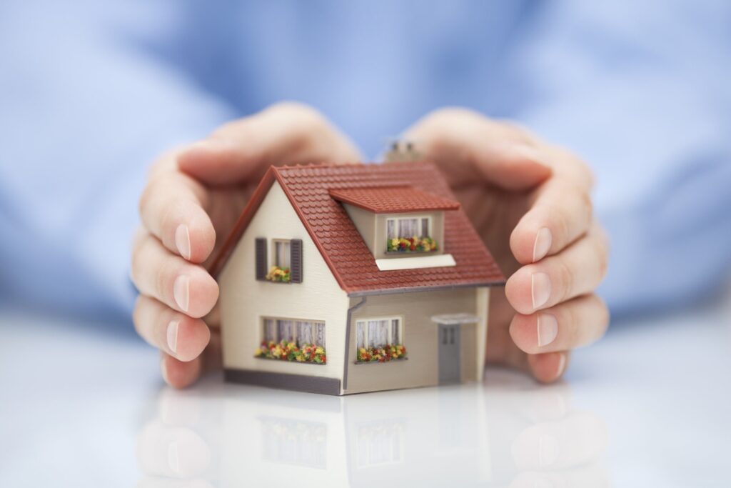 A person gently cradles a small house in their hands.