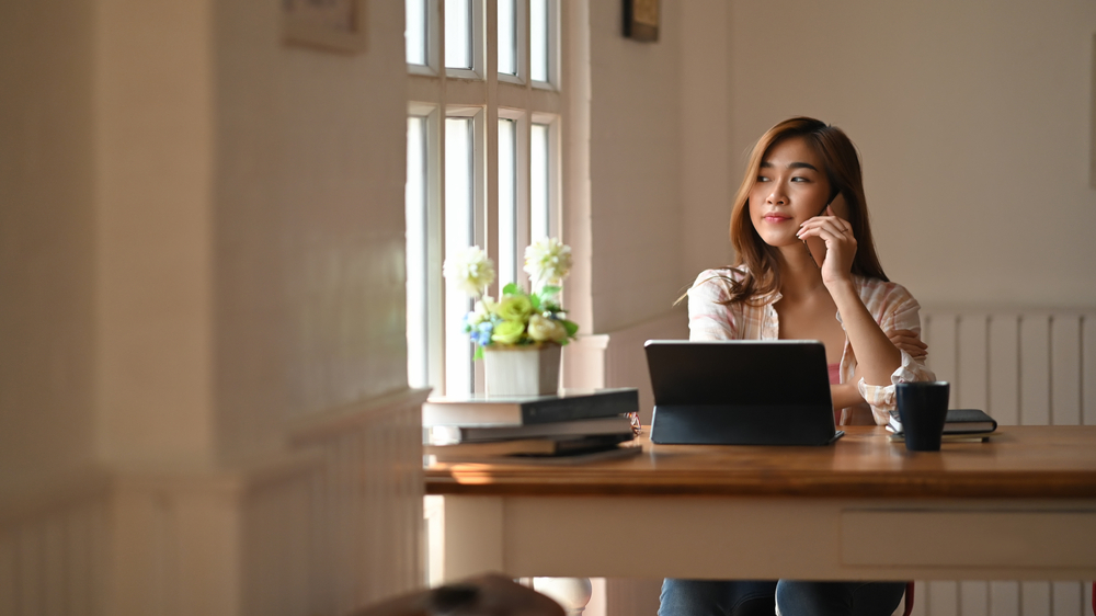 A woman seated at a table, using a laptop and phone.