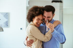 A man and woman smile and hug while holding a toothbrush.