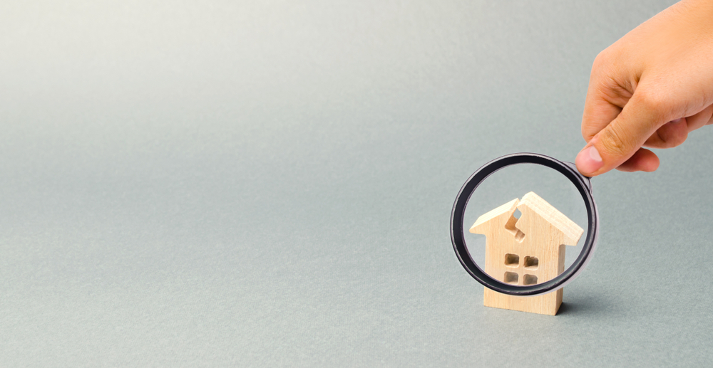 Hand holding a magnifying glass over a small house model.