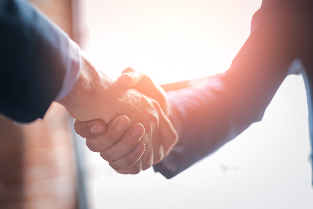Two business professionals shaking hands by a large window.