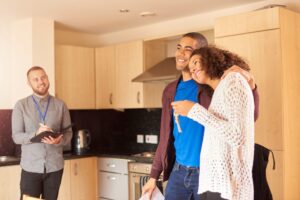 Smiling couple receiving keys to a new property while an agent observes during the handover.