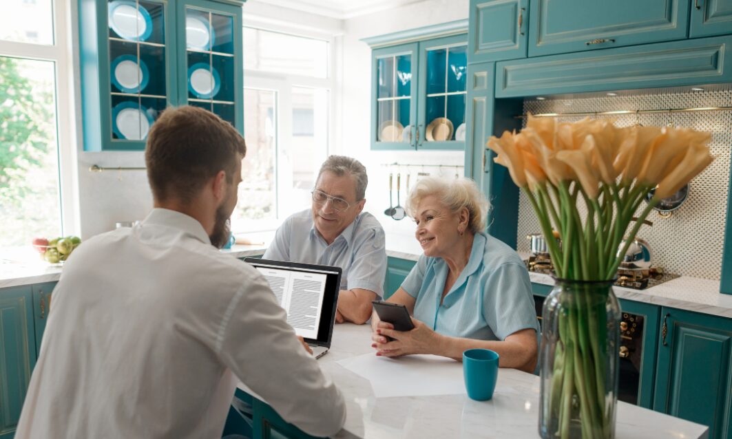 Estate agent discussing property details with homeowners at a kitchen table, representing Long Ashton property market trends and valuations