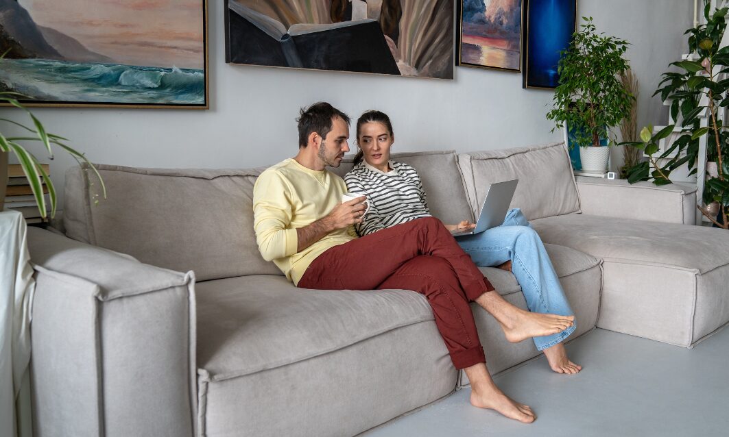 Young couple sitting on a sofa reviewing rental property details on a laptop in Southville