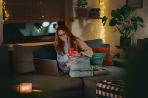 Woman sitting on a sofa with a laptop and mug, representing homeowners researching the Long Ashton property market before selling.