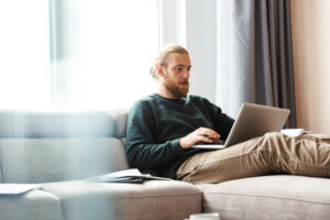 Man sitting on a sofa using a laptop, representing homeowners checking their Bishopsworth property value in 2025.